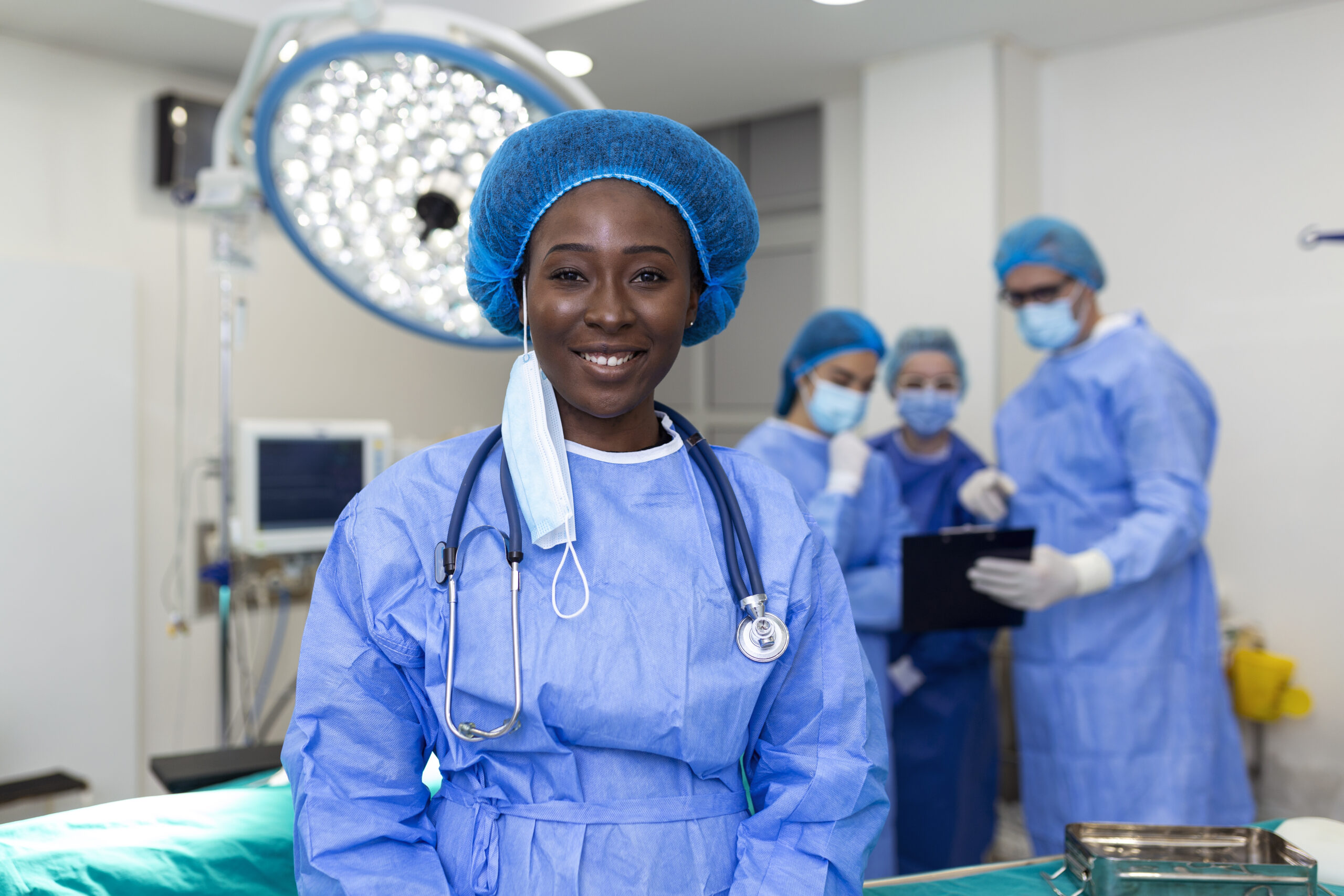 Portrait of happy African American woman surgeon standing in operating room, ready to work on a patient. Female medical worker in surgical uniform in operation theater.